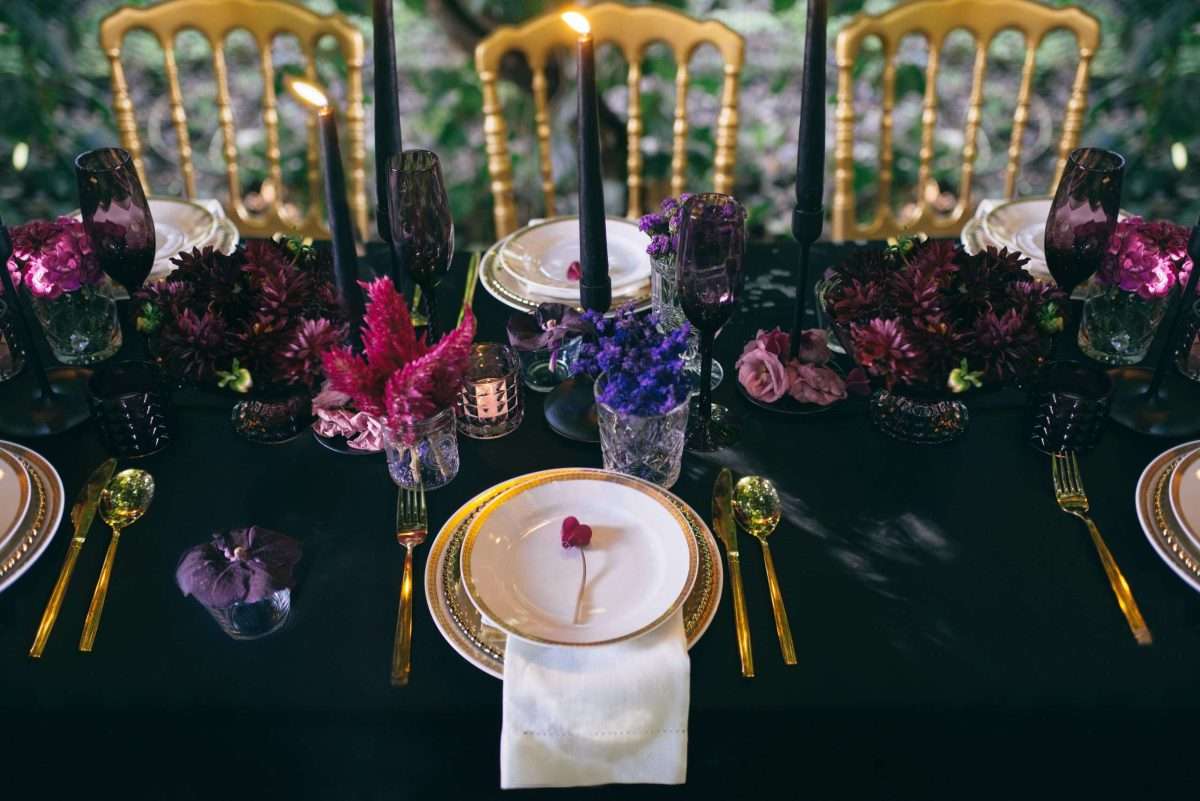 Allestimento tavola per matrimonio dai toni profondi: tovaglia blu profondo, fiori color borgogna, fuxia e viola