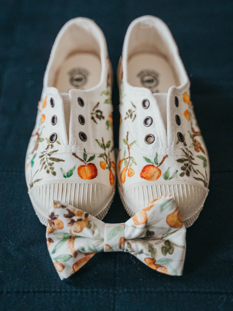 Primo piano del papillon personalizzato per lo sposo e le scarpine per in figlio, realizzate artigianalmente, dipinte con il pattern dei frutti antichi, fil rouge del matrimonio
