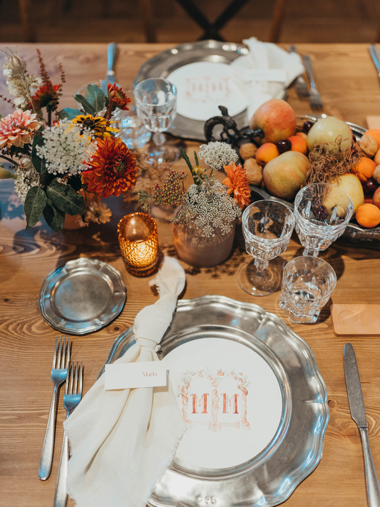 Un primo piano della tavola, con allestimento floreale centrale, la mise en place e menu tondo a coprire il sottopiatto in peltro personalizzato con il monogramma rappresentate un doppio arco con all'interno le iniziali MM.