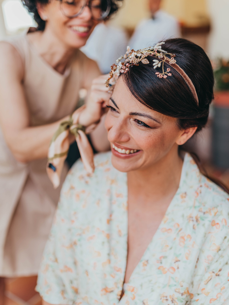 un primo piano della sposa con vestaglia personalizzata con il pattern dei frutti antichi mentre Maria le sistema la coroncina in testa