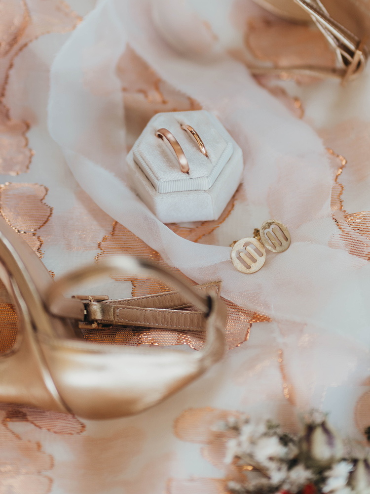 Sullo sfondo il tessuto del mantello ricamato con i fili color rame studiato appositamente per lei, era ispirato alla nostra musa ispiratrice, virt&ugrave; della giustizia, sopra appoggiate le scarpe della sposa color champagne, gli anelli in oro rosa, e gli orecchini personalizzati con l'iniziale M.