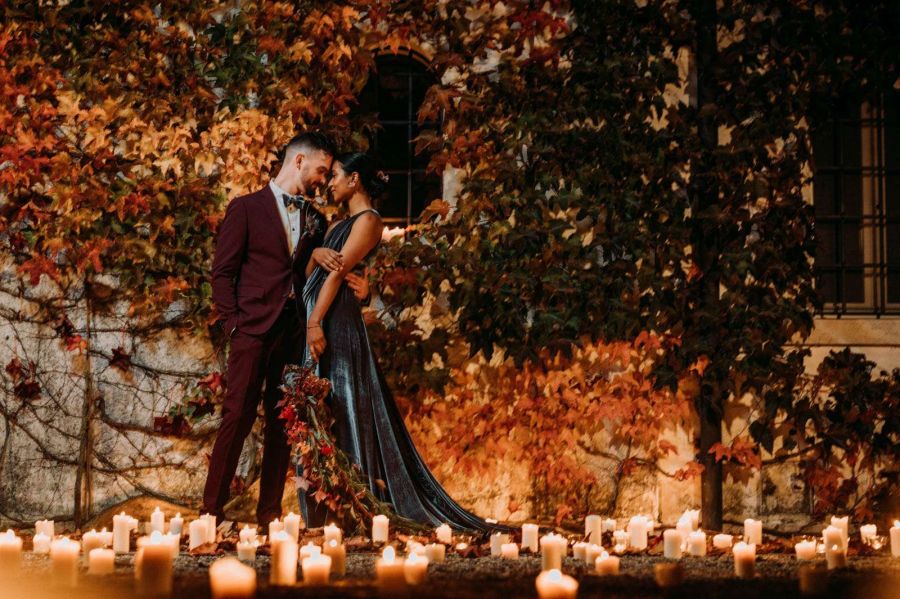 Foto sposi con vestiti entrabi di color borgogna, si stanno abbracciando e baciando e nello sfondo un arco di fiori e piante che partendo dalla sinistra formano un gradiente che va dal giallo al bordeaux - Maria Mayer wedding & event designer a treviso, Veneto e tutta Italia